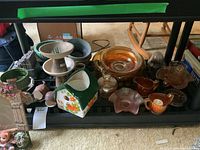 Shelf displaying various items including carnival glass bowls, ceramic cream and sugar set, lidded dish with deer figurine, measuring cup, and decorative picture frame.