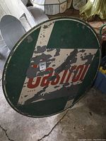 Full view of the large round painted metal Castrol sign showing significant paint wear and surface damage.