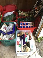 Five plastic storage totes filled with assorted Christmas decorations visible including garlands, ornaments, floral picks, and a boxed light show.