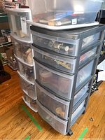 Two plastic storage drawer units with transparent front drawers visible, filled with various craft supplies including glue, string, paint tubes, and stamps.