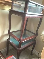 Stacked view of two wood end tables with glass display cases on top, showing curved legs and dark wood finish.