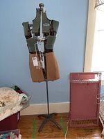 Full view of White brand adjustable dress form on metal stand, next to bins and furniture.