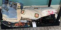 Photo showing folded assorted linens including knit floral blanket and embroidered tablecloths on shelf.