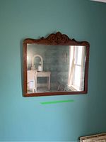 Front view of wooden framed mirror mounted on blue wall, showing decorative carved top and reflective surface with visible dust and spots.