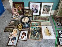 Overview of various framed prints and plates laid on carpet, featuring children, animals, and scenic paintings.