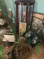 Photo showing a small curved wooden curio cabinet, two green vine patterned glass bottles, framed photos, decorative figurines, and an iron door stop on the floor clustered together