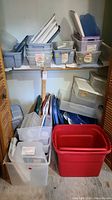 Closet shelf filled with various plastic storage bins and corresponding lids in multiple colors and sizes.