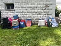 Wide view of assorted colorful plastic tote bins stacked and arranged against a stone wall on grass.
