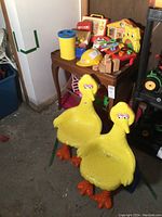 Pair of yellow Big Bird plastic children's chairs with molded wings and orange feet in basement setting