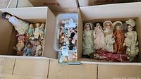 Overview of two boxes containing twelve dolls of varying sizes and a plastic bin of loose parts