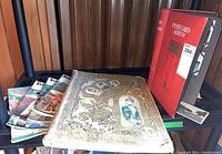 Photo showing postcard album with ornate gold cover, a red postcard album, and a stack of Toronto Week magazines.