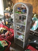 Front view of white wicker shelf stocked with various items, showing structure and condition.