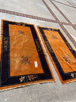 Two similar Asian style rugs side by side, showing overall design and color scheme with floral borders and fringes.