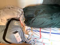 Photo of folded inflatable green AeroBed with attached label and bedding draped over and around it