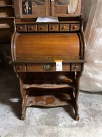 Front view of the antique wooden roll-top desk showing drawers, shelves, and roll-top cover closed.