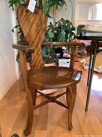 Full view of wooden carved chair showing curved armrests, contoured seat, and decorative backrest.