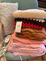 Full view of lot of folded blankets including electric blanket controller and crocheted blankets on a teal chair.