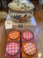 Photo showing enameled soup pot on box with four colorful Easter-themed small cans with checkered lids arranged in front