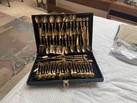62-piece set of gold-toned flatware including spoons, forks, and knives arranged in black fitted case