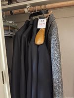 Photo shows four jackets hanging in a closet including three black women's jackets size petite 16 and one grey tweed men's jacket with wooden hanger tag.