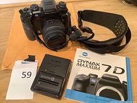 Overall view showing Konica Minolta camera, Sony battery charger, instruction manual, and neck strap on table.