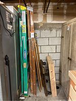 Photo showing multiple ladders and an old wooden dolly in storage, including a green Werner fiberglass ladder and wooden step ladders