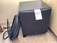 Front angled view of the black Martin Logan subwoofer showing the textured grille and logo, with cable visible beside it.