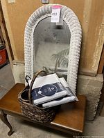 Wooden piano bench with a white wicker framed mirror behind it, wine caddy basket on the bench containing two packs of men's v-neck t-shirts