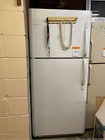Full view of the exterior front of the white refrigerator with top freezer and bottom fridge, showing two handles on the right side and items hanging on the freezer door.