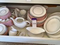 Photo showing various Royal Doulton china plates, a sugar bowl, creamer, gravy boat, and bowls, stacked and arranged in a drawer with pink padded storage cases.