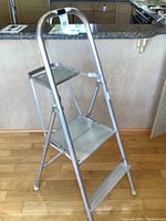 Photo of small aluminum step ladder unfolded showing two wide steps and curved top handle.