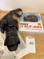 Overhead shot of camera body with attached lens, lens hood, guidebook slipcase and papers