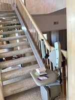 Full view of the stair lift chair and transparent rail installed on carpeted stairs with wooden banister.