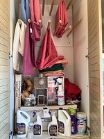 Tablecloths in various colors hanging and folded, with Bona cleaning bottles and Lysol container on shelf.