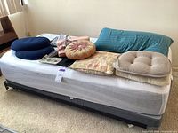 Photo showing twin size bed with mattress, foundation, and several assorted pillows piled on top.