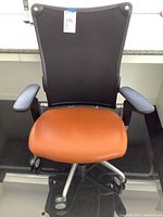 Front view of Allsteel office chair showing mesh back, orange cushioned seat, adjustable armrests, and silver 5-star base with casters.