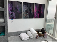 Three framed art prints with purple, pink, aqua abstract floral or coral designs hung on wall above bathtub.