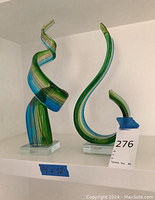 Both sculptures on white shelf with size tape and lot tag visible