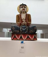 Front view of painted wooden Buddha statue seated on lotus base