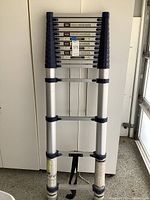 Aluminum telescoping ladder fully collapsed, front view showing strap and rubber feet