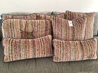 Six cushions arranged on gray sofa: four square cushions with multicolored stripe pattern and two rectangular lumbar cushions showing patterned side