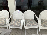 Front view of five white resin wicker patio chairs with patterned cushions aligned on deck