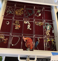 Drawer grid showing 16 compartments with costume jewelry pieces on red velvet liner.
