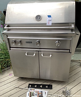 Closed front view of grill showing stainless steel exterior, control panel with three knobs, lid thermometer and cabinet doors.