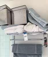 Front view of lot on wall-mounted chrome rack showing two wastebaskets on top shelf with folded bath mats and towels below.