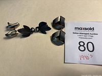 Three pairs of antique earrings laid out on beige surface with auction card indicating 1940s date.