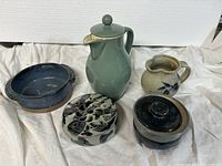 Photo showing a green Denby ceramic pitcher with lid, beige Robin Cage pitcher, blue bowl, round potpourri dish, and covered jar.