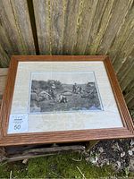 Full view of framed antique photogravure engraving on wood surface outdoors.