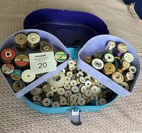 Open plastic carry case showing upper tier with assorted vintage and modern spools of thread including brands like Coats & Clark and Sewatec, plus lower tray filled with white bobbins.