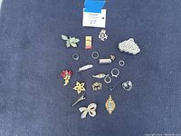 Full view of all costume jewelry pieces arranged on a dark fabric background. Includes multiple pins, rings, and a hair clip.